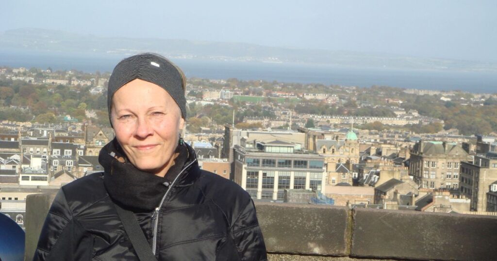 Mary Emmer standing at Edinburgh Castle’s overlook with panoramic views of Edinburgh and the Firth of Forth behind her.