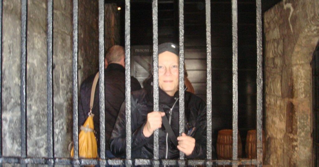 Mary Emmer inside a barred prison cell at Edinburgh Castle during her visit, illustrating the historic vaults used to hold prisoners of war.
